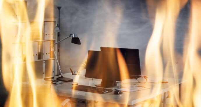Office desk with computer monitors surrounded by flames