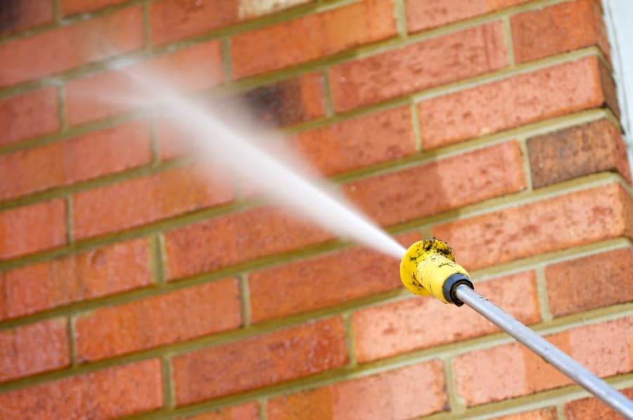 Closeup of pressure washer hose spraying brick wall