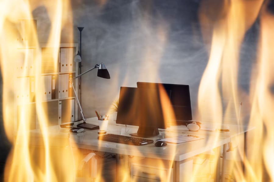 Office desk with computer monitors surrounded by flames