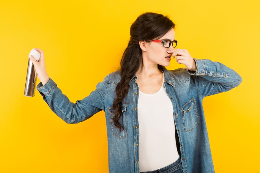 Woman spraying air freshener and plugging nose