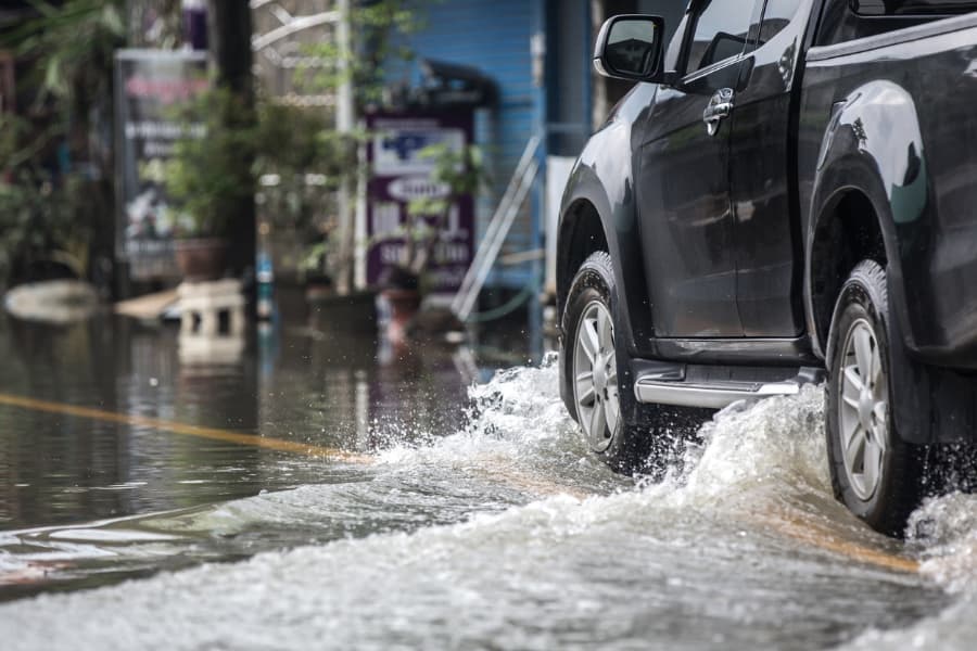 Black pickup truck driving through flooded street on main road with commercial businesses