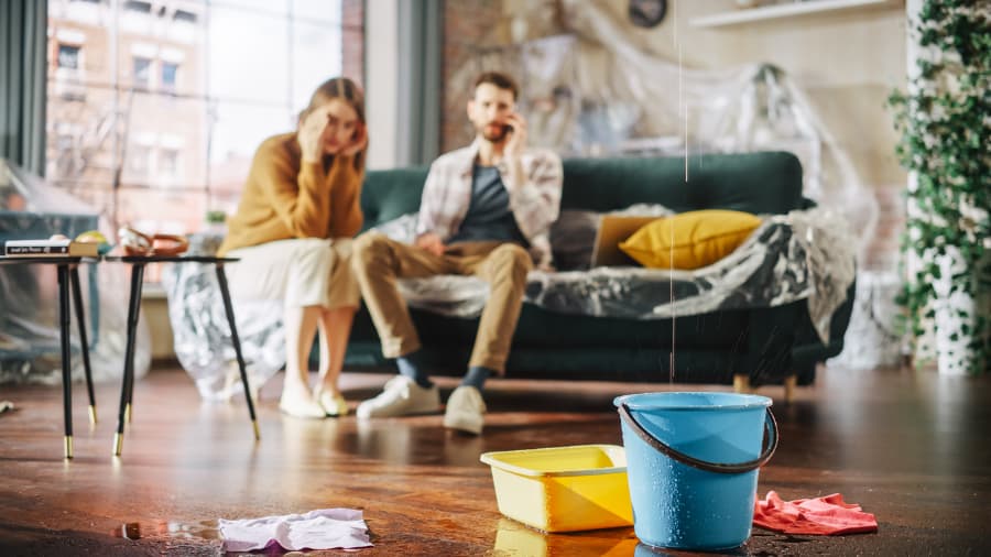 Couple sitting on couch in disbelief as ceiling leaks water from burst pipe