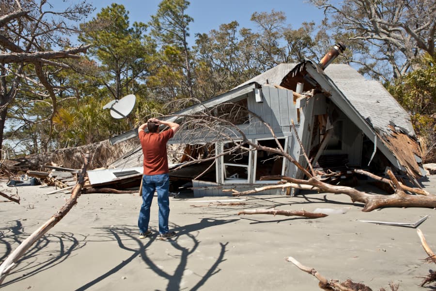 Man puts hands on head in gesture of shock while surveying destroyed house