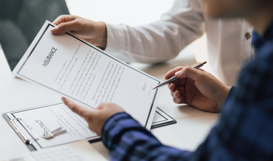 Policyholder holding form and pen reviewing insurance information with broker