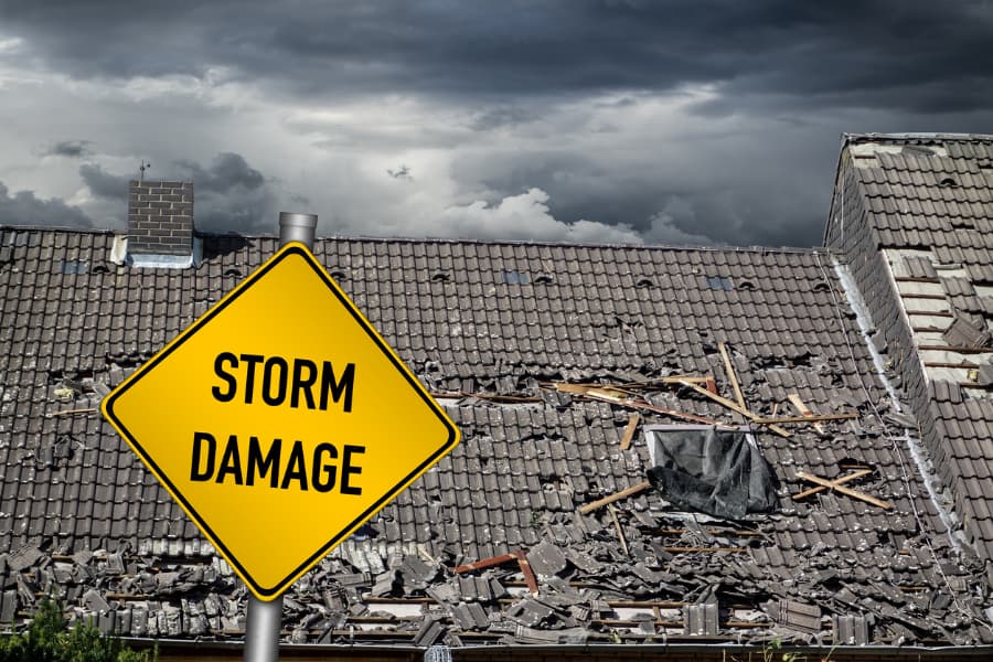 A roof damaged by heavy winds, with a “Storm Damage” warning sign posted