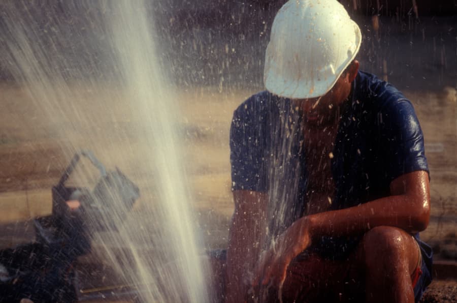 Worker in hard hat examines gushing water leak at commercial property