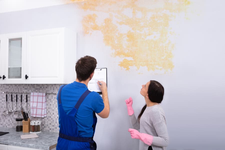 Young worker writing on clipboard with woman standing in kitchen